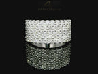 Close-up image of a white gold ring encrusted with multiple small diamonds, reflecting light on a black surface. The ring features a pattern of closely set diamonds creating a sparkling effect.