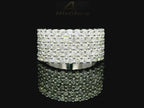 Close-up image of a white gold ring encrusted with multiple small diamonds, reflecting light on a black surface. The ring features a pattern of closely set diamonds creating a sparkling effect.